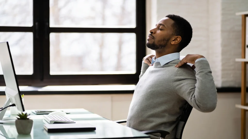 Man sitting at his desk gently pulling his shoulders back to decompress tension during a short workday reset.